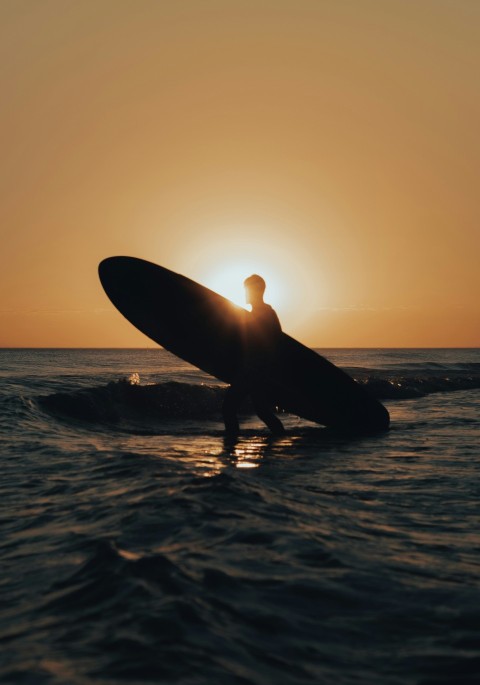 a man holding a surfboard in the ocean at sunset