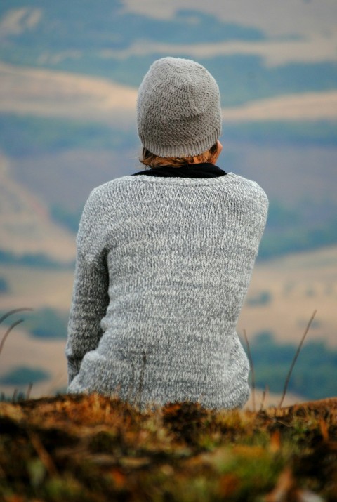 person in gray sweater sitting on green grass overlooking mountian gXl 75