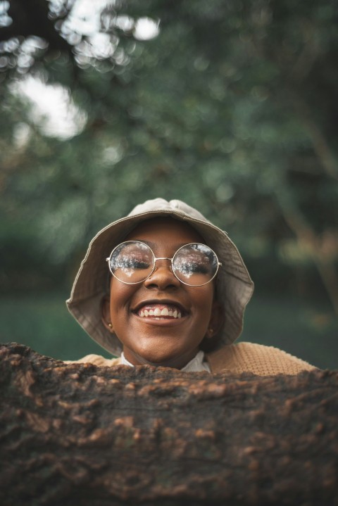 a woman wearing a hat and glasses standing in front of a tree