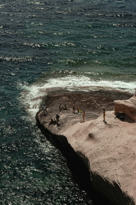 a group of people standing on top of a cliff next to the ocean E36vYzl