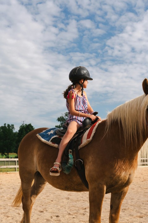 a young girl riding a horse in a dirt field