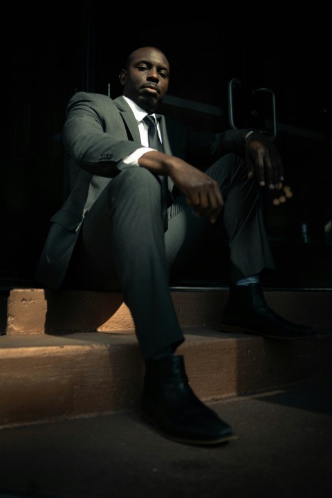 man in black blazer and gray pants sitting on brown wooden bench