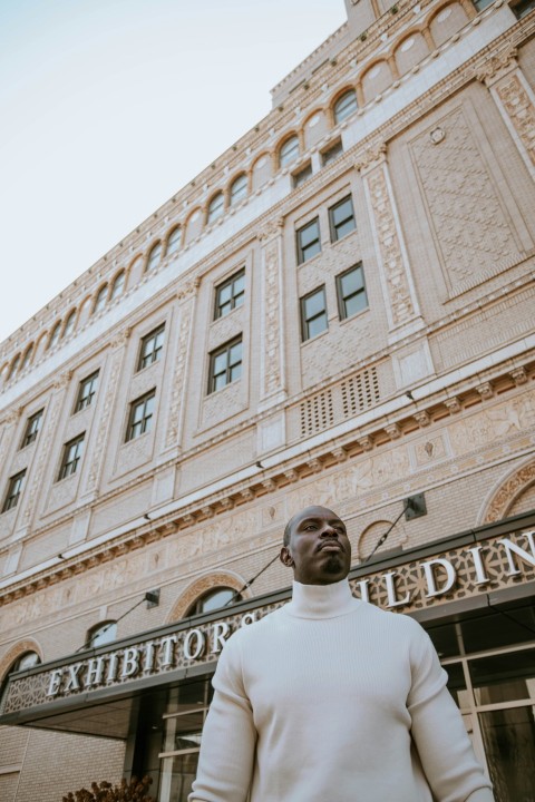 man in white crew neck shirt standing near white concrete building during daytime