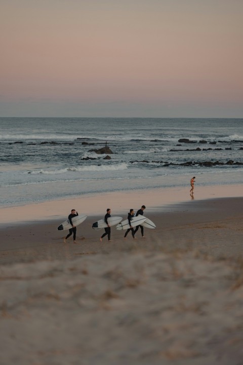 a group of people walking along a beach holding surfboards