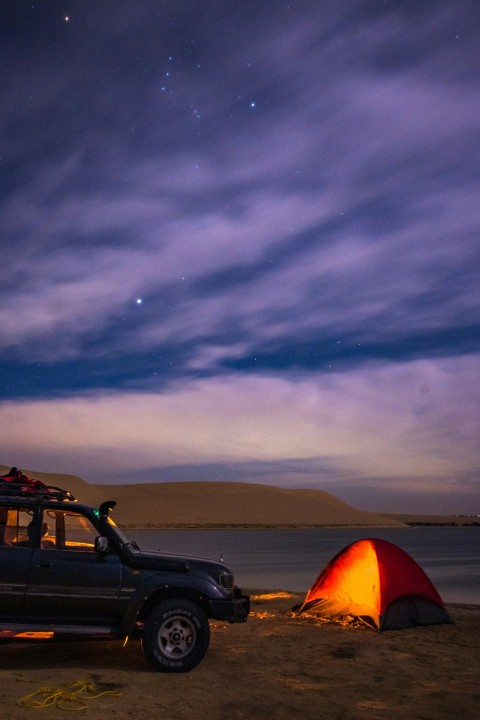 a truck parked on a beach next to a tent