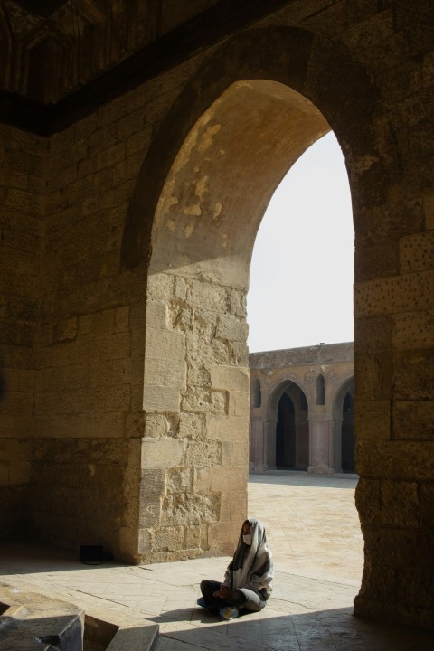 a person sitting on the ground under an arch Rqa