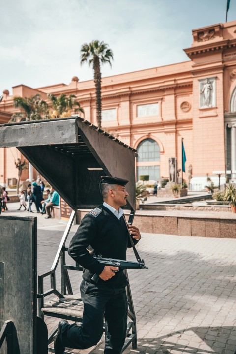 man standing carrying smg near building