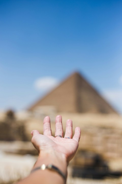 a persons hand reaching out towards a pyramid