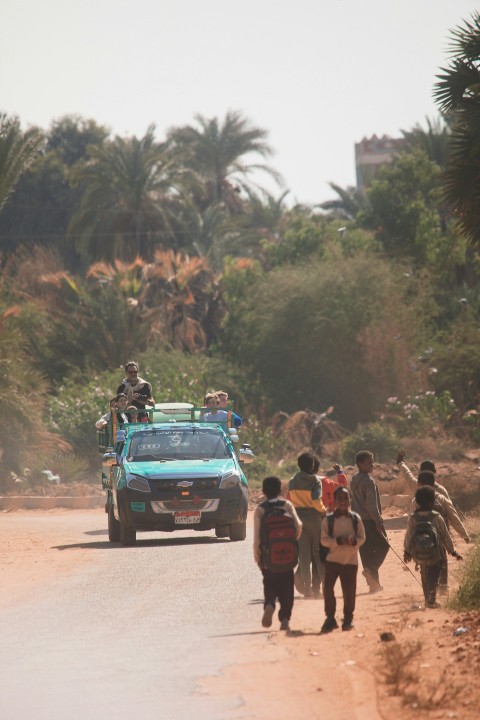 a group of people walking down a dirt road vaZ