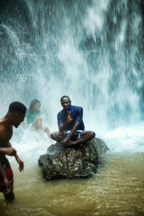 a man sitting on a rock in front of a waterfall