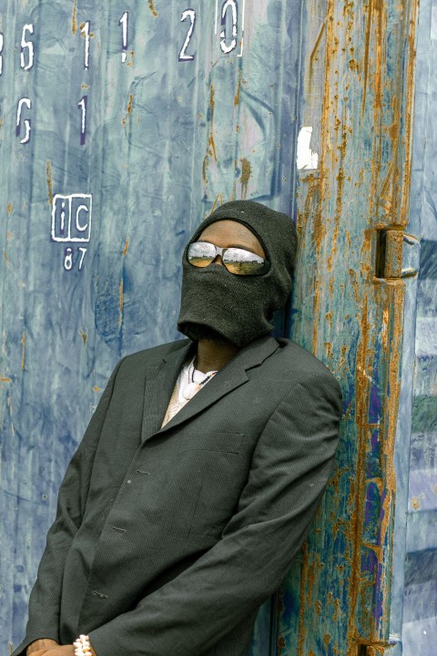 a man in a suit and mask leaning against a wall