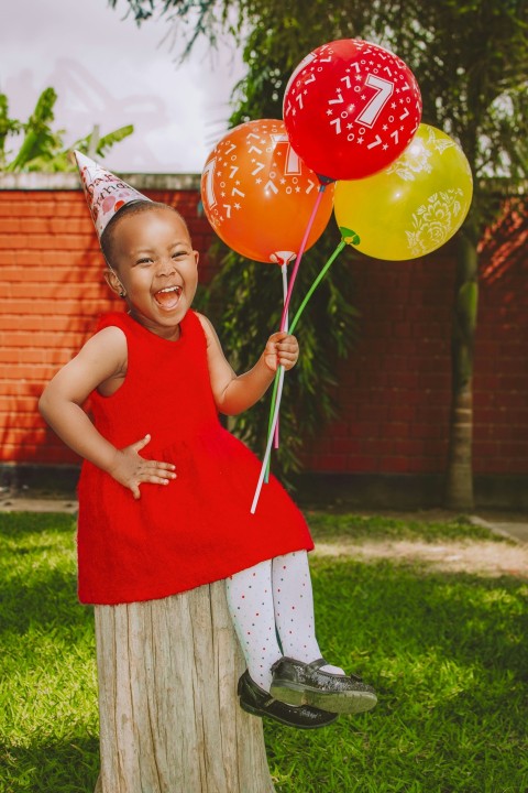 a little girl in a red dress holding some balloons