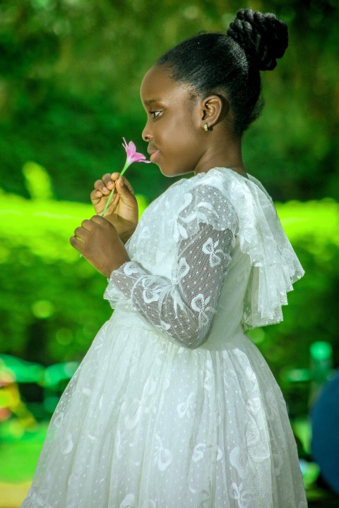 a woman in a white dress smelling a flower