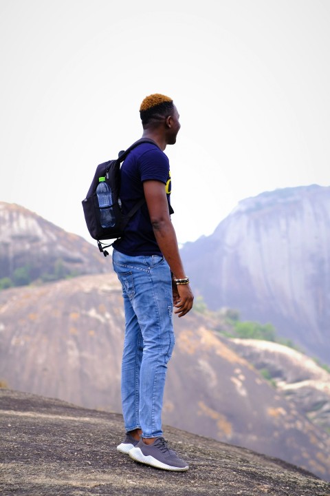 man in blue denim jeans with black backpack standing on gray concrete road during daytime