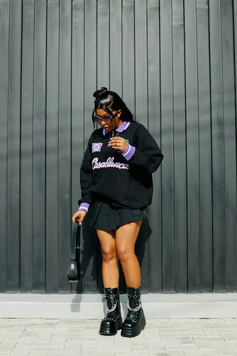 a woman in a black sweater and boots leaning against a wall