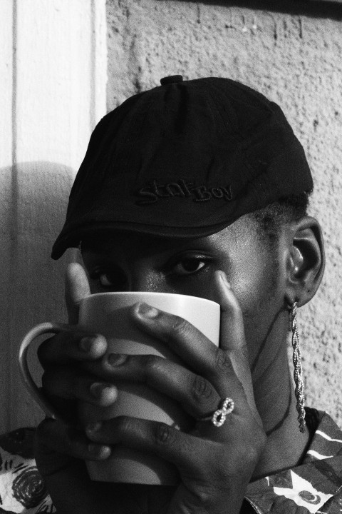 man in black hat and silver necklace holding white ceramic mug