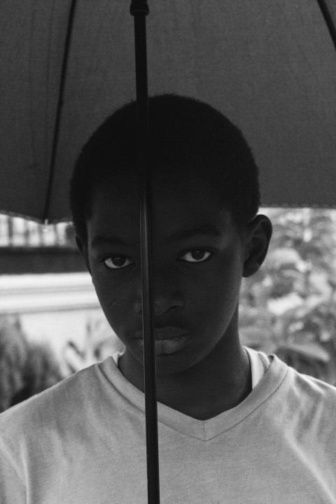 grayscale photo of boy in crew neck shirt holding umbrella