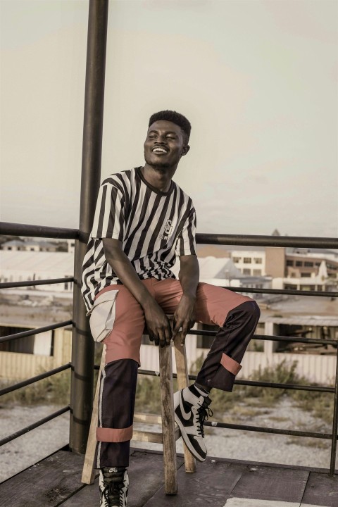 man in black and white stripe crew neck t shirt and brown pants sitting on brown