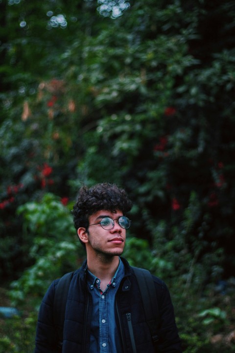 a man wearing glasses standing in front of a forest