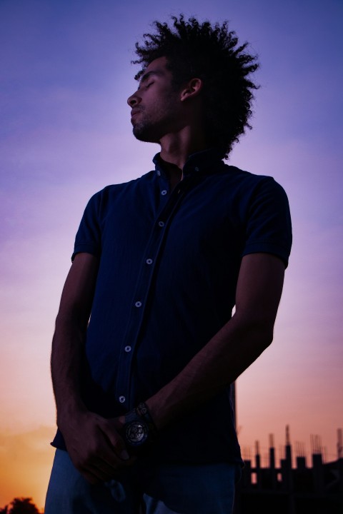 man in black button up shirt standing during sunset AB