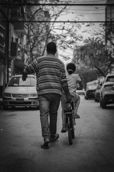 man in striped shirt and denim jeans walking on sidewalk in grayscale photography