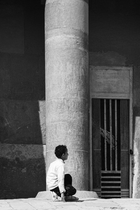 a young boy sitting on the ground in front of a building