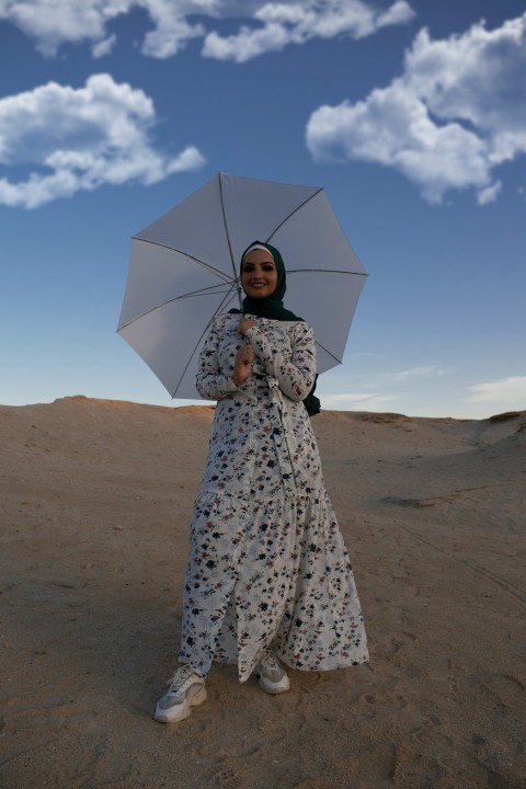 woman in white and black floral dress holding umbrella walking on brown sand during daytime