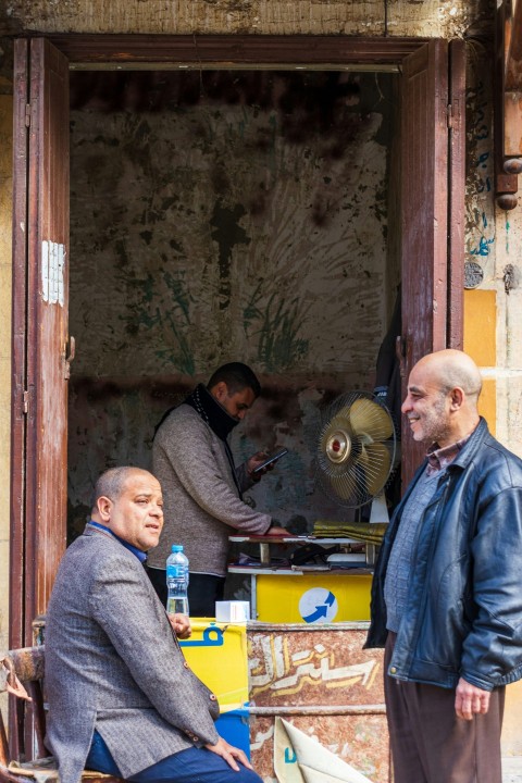 two men standing outside of a building with a fan AD3WS