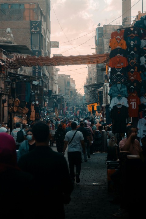 a crowd of people walking down a street with buildings on either side 0xjdc7x