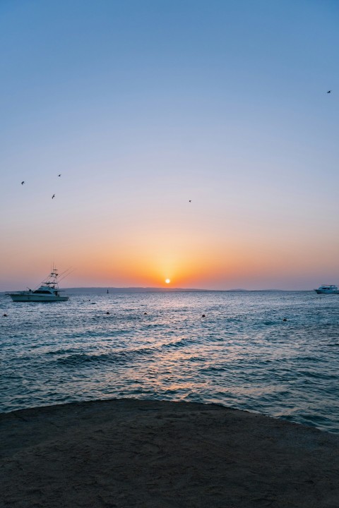 the sun is setting over the ocean with boats in the water