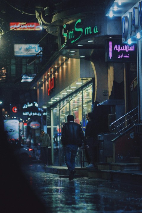 man in black jacket walking on sidewalk during night time