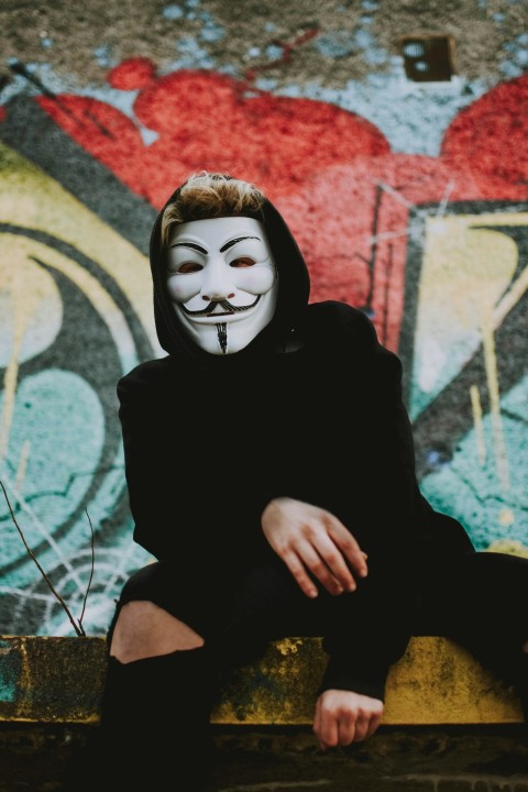 man wearing guy fawkes mask sitting on yellow concrete bench