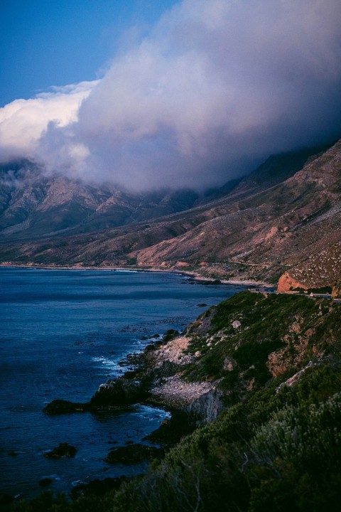 brown and green mountain beside blue sea under white clouds during daytime