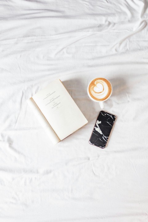 white ceramic mug beside white book on white textile