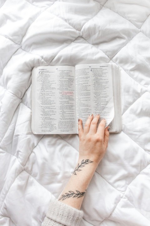 person reading book on white bed