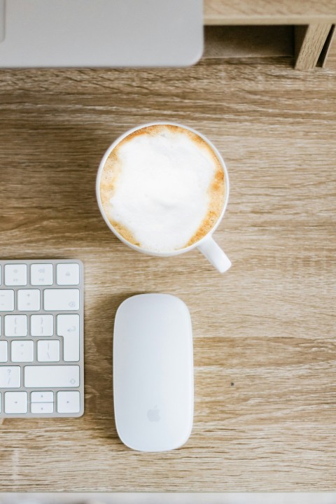 white apple magic mouse beside white ceramic mug with brown liquid