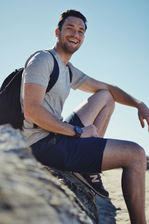 smiling man sitting on gray rock at daytime NDCy2