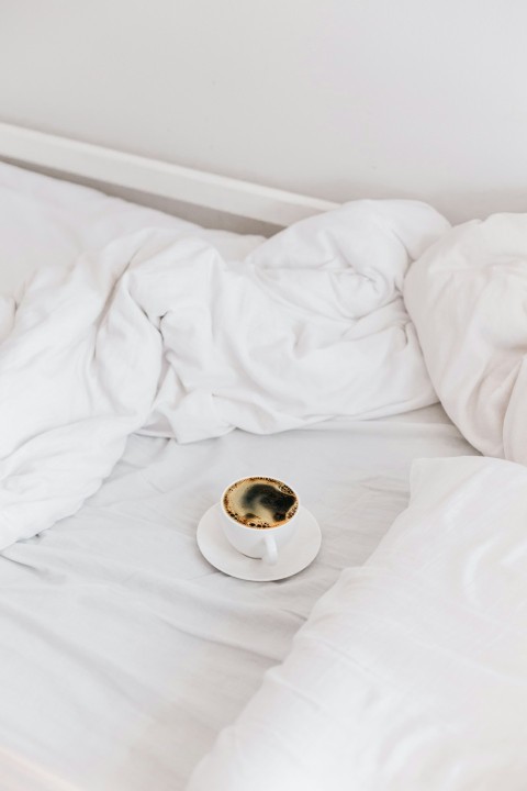 a cup of coffee sitting on top of a white bed