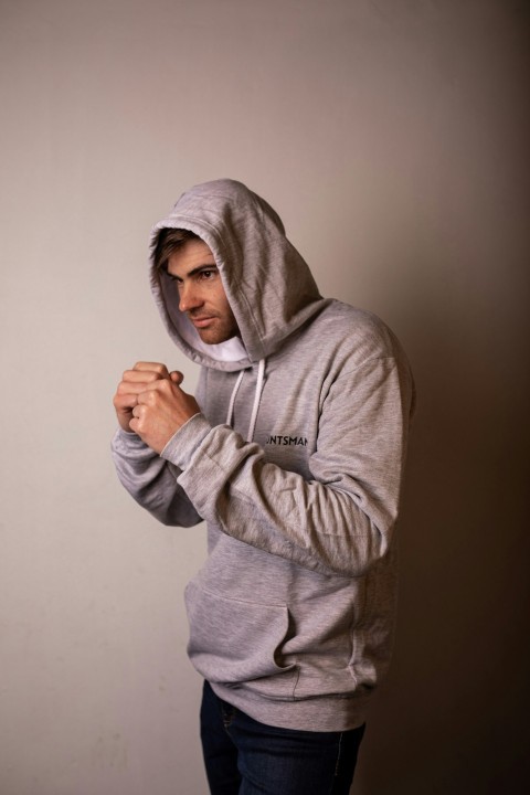 a man in a gray hoodie standing in front of a wall