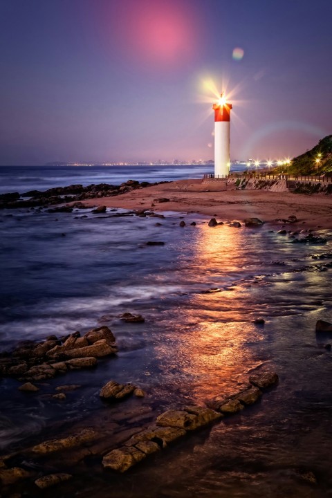 white and red lighthouse on seashore during sunset