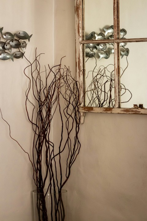 a vase with branches in front of a mirror