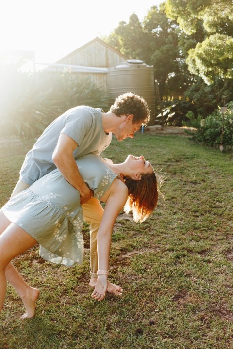 man in gray shirt kissing woman in white dress on green grass field during daytime