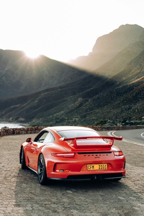 a red sports car on a road with mountains in the background