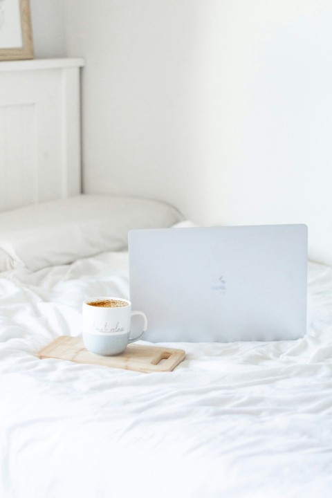 white ceramic mug on white textile beside silver macbook