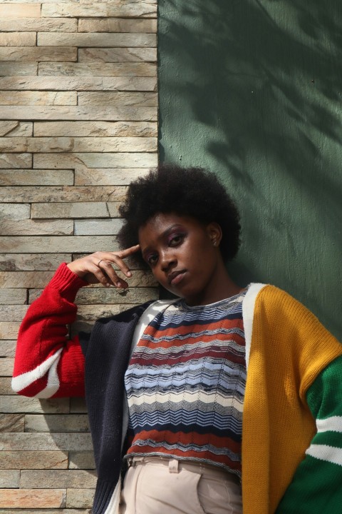 a woman leaning against a brick wall wearing a colorful sweater