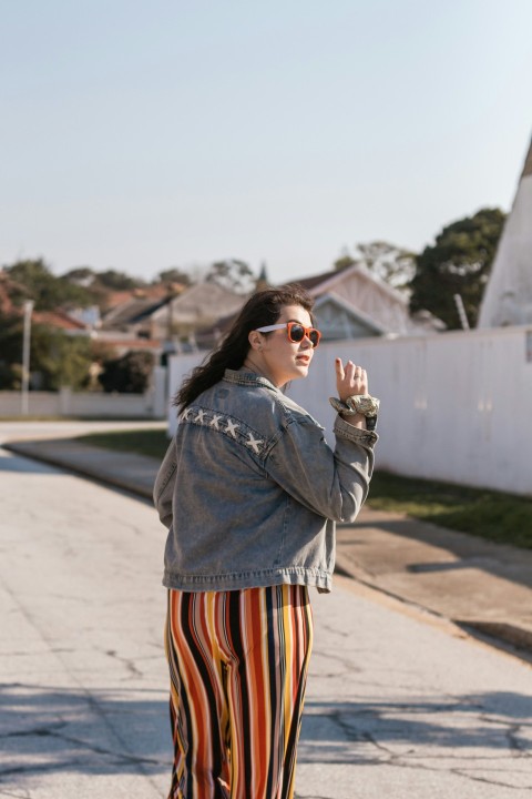 woman in black jacket and orange white and black striped skirt standing on road during daytime