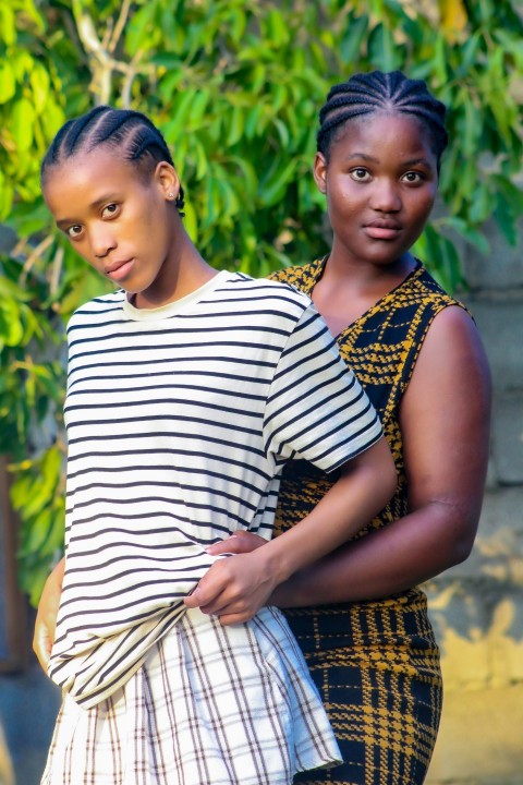 two women standing next to each other in front of a tree