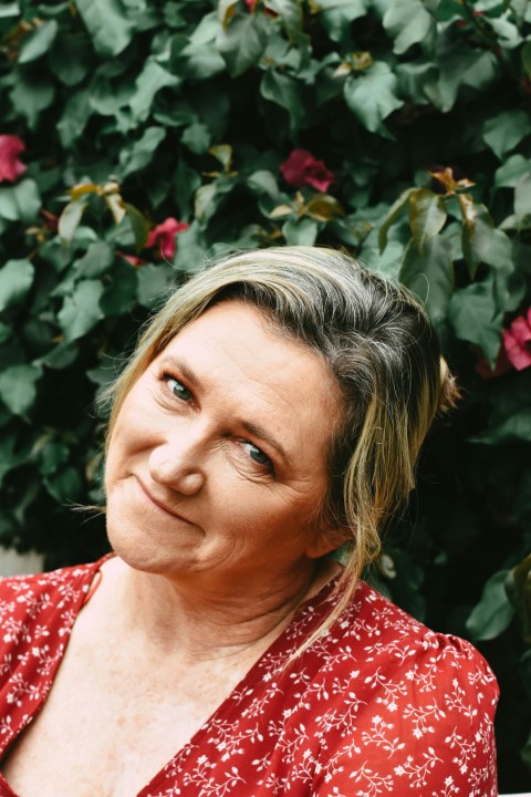 a woman in a red shirt sitting in front of a bush