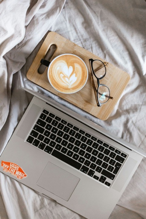 macbook pro beside black framed eyeglasses on white textile