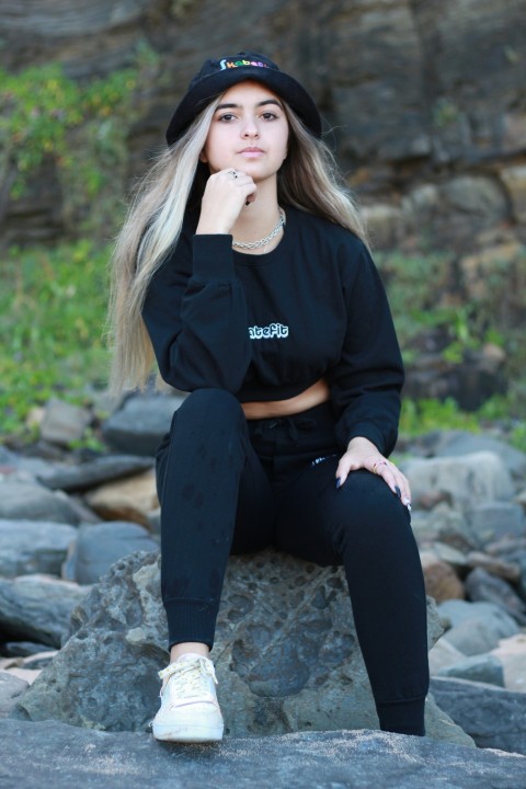 a woman sitting on a rock wearing a black sweatshirt and sweatpants MESu3xqqA